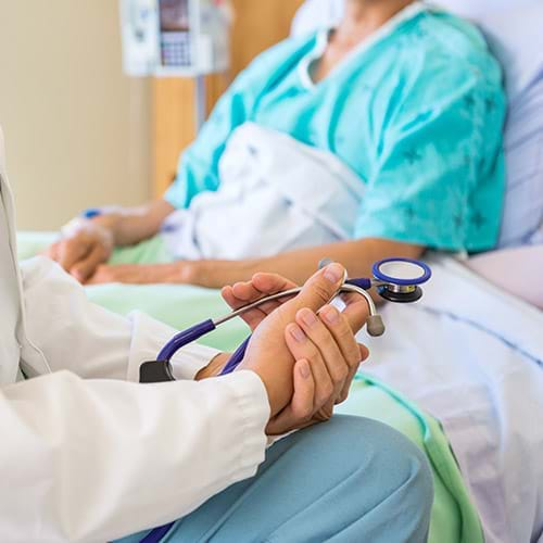 A woman laying on a hospital bed and a doctor sitting on the bed with a stethoscope