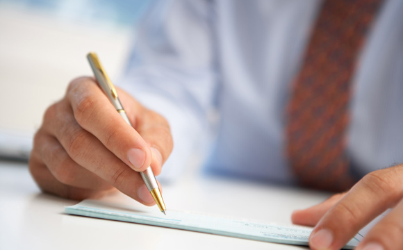 A closeup of a man in a tie signing a document with a metal pen.
