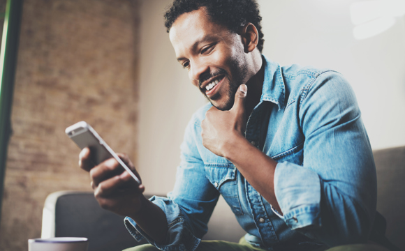 A man smiling as he checks his mobile phone and strokes his chin.