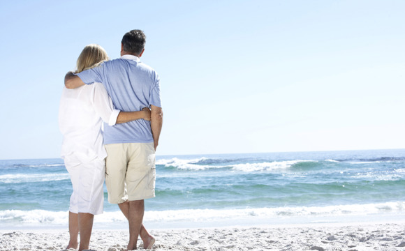 An older couple on the beach staring out at the water.