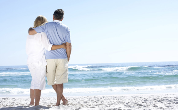 An older couple on the beach staring out at the water.