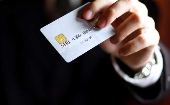 A close up of a debit card held by a man in a suit.