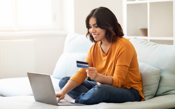 A woman with a laptop on her bed making a financial transaction in a bright sunlit room.