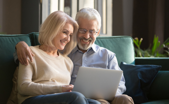 An older couple smiling as they look at their laptop.