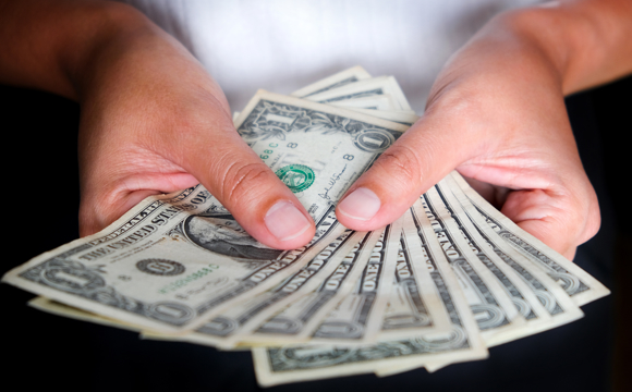 A closeup of two hands holding a fanned collection of dollar bills.