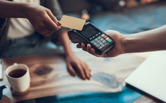 A customer's hand making a contactless purchase with a credit card at a coffee shop register.