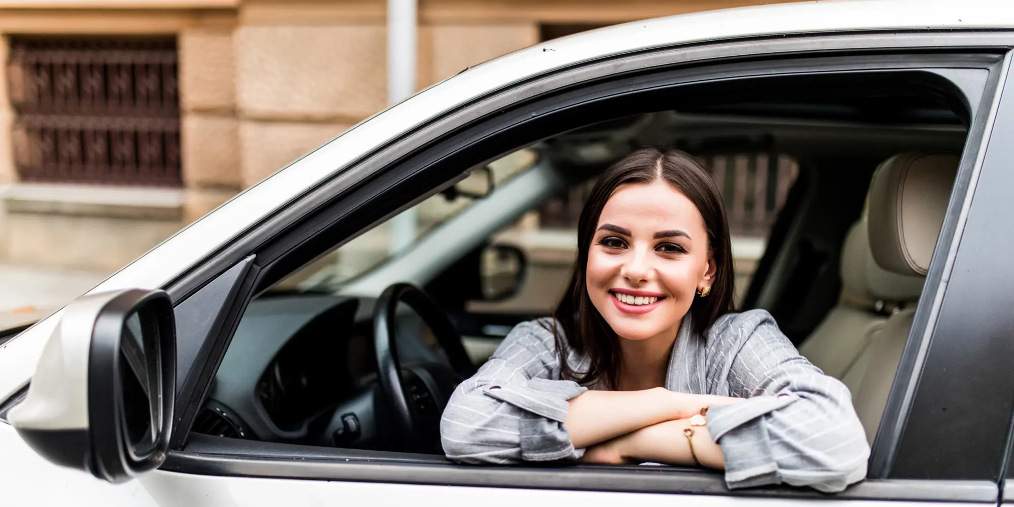 New car buyer happily sitting in the drivers seat smiling out the window
