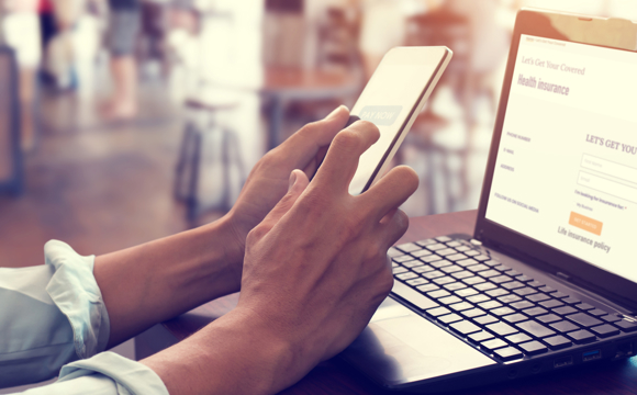 A closeup of some hands using a phone at a cafe over a laptop.