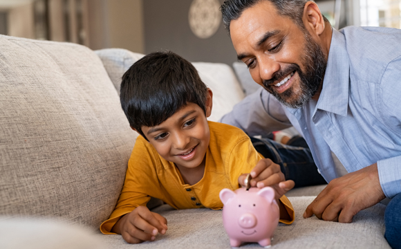 A dad helping his son add money to his piggy bank.